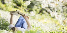 Woman reading book in grass under tree with white blossoms